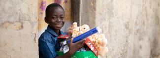 Boy smiles with shoebox gift and toy giraffe