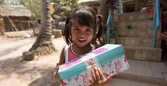 Child smiling holding blue and white shoebox gift