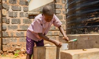 A STUDENT IN KENYA TESTS THE WATER SYSTEM, PREPARING TO ENJOY A DRINK OF CLEAN WATER.