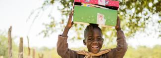 Child smiles and holds shoebox above head