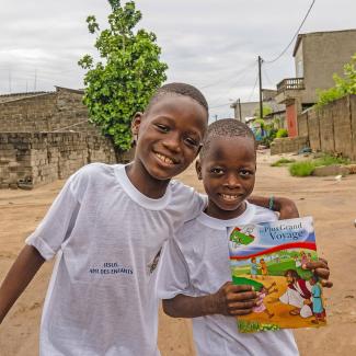 Kids in Benin smile for a photo with The Greatest Journey in hand