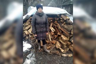 Tetiana standing in front of a pile of firewood