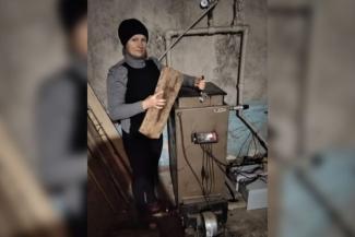 Tetiana holding a piece of firewood beside a wood stove